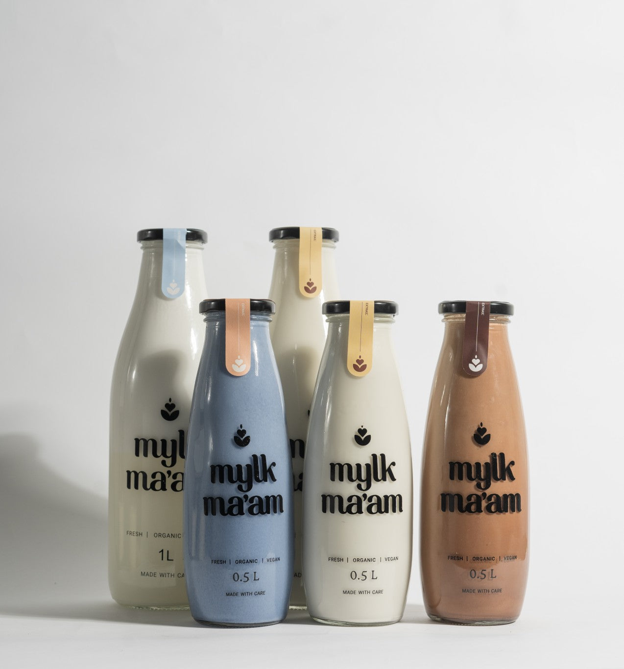 A series of four bottles of Mylk Ma'am oat drink in different colors (blue, white, brown, and black).